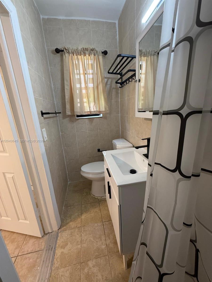 A small bathroom features beige tiled walls, a white vanity, and a black faucet — 1301 NE 110th St # 3, Miami FL 33161, MIAMI, FL