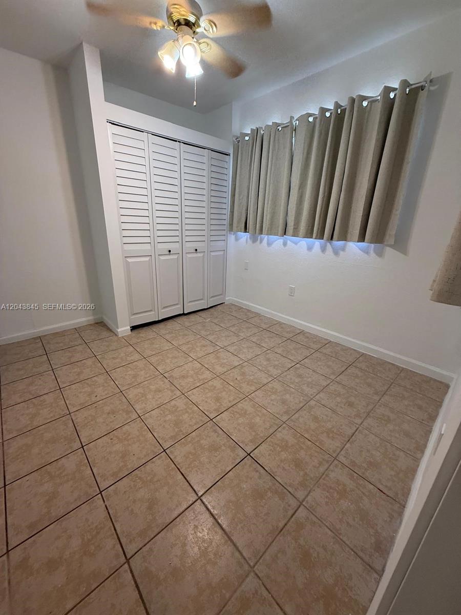 An empty room features beige tile flooring, white walls, a ceiling fan, and louvered closet doors — 1301 NE 110th St # 3, Miami FL 33161, MIAMI, FL
