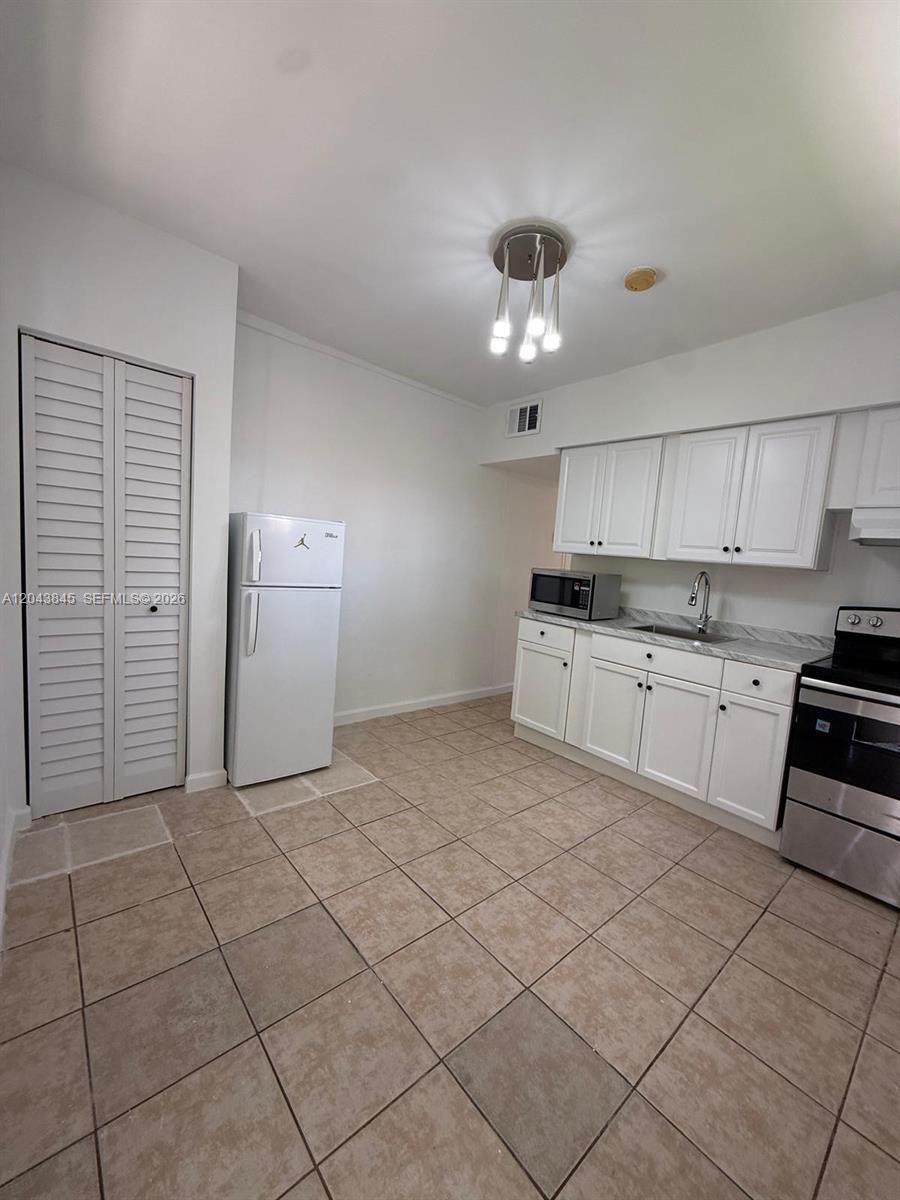 A kitchen features white cabinets, stainless steel appliances, and light-colored tile flooring — 1301 NE 110th St # 3, Miami FL 33161, MIAMI, FL