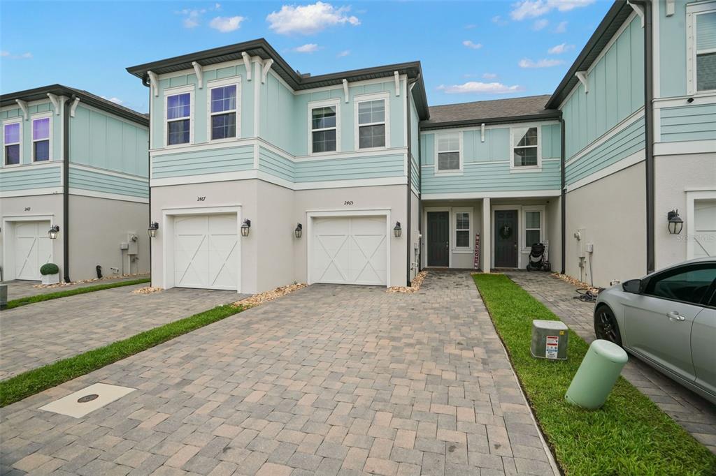 A row of two-story townhomes with light blue siding, white garages, and paver driveways — 2465 FOGGY CREEK CIRCLE, CLEARWATER, FL