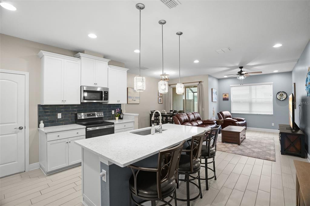 A kitchen with white cabinets, a quartz island, and a dark tile backsplash opens to a living area — 2465 FOGGY CREEK CIRCLE, CLEARWATER, FL