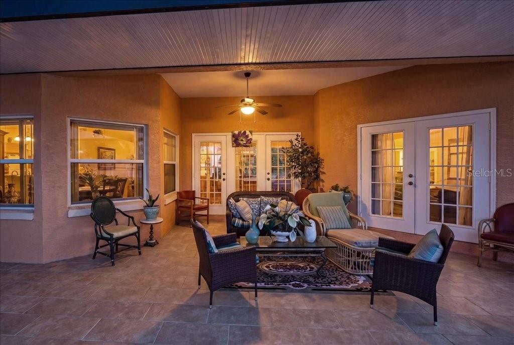 A covered patio features tiled flooring, outdoor furniture, and multiple glass-paned doors at night — 52 UPSHIRE PATH, PALM COAST, FL