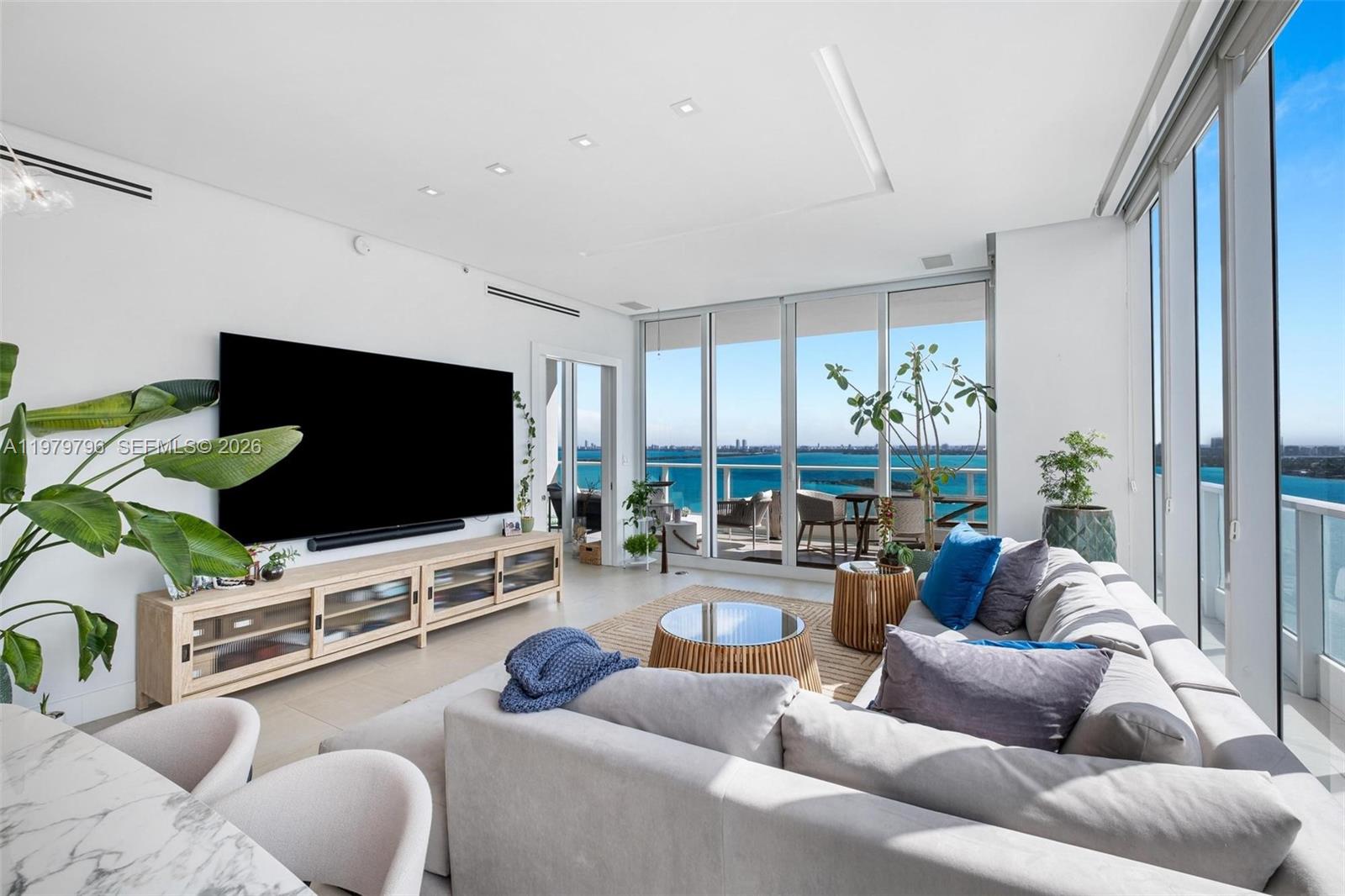 A bright living room features a large television, light wood media console, and floor-to-ceiling windows — 2020 N Bayshore Dr # 2510, Miami FL 33137, MIAMI, FL