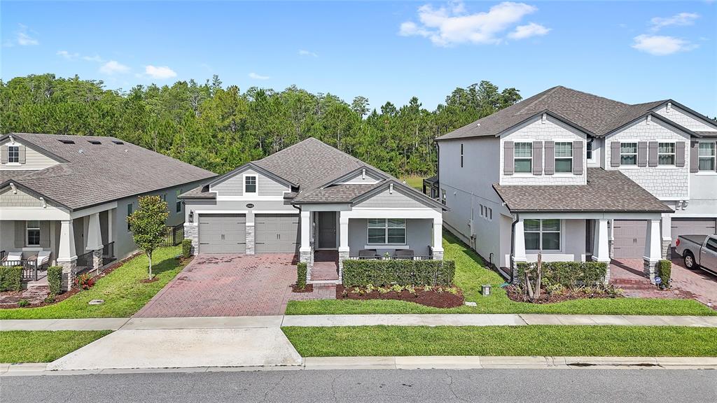 An exterior view of three suburban houses with gray siding, brick driveways, and manicured lawns — 12410 ENCORE AT OVATION WAY, WINTER GARDEN, FL