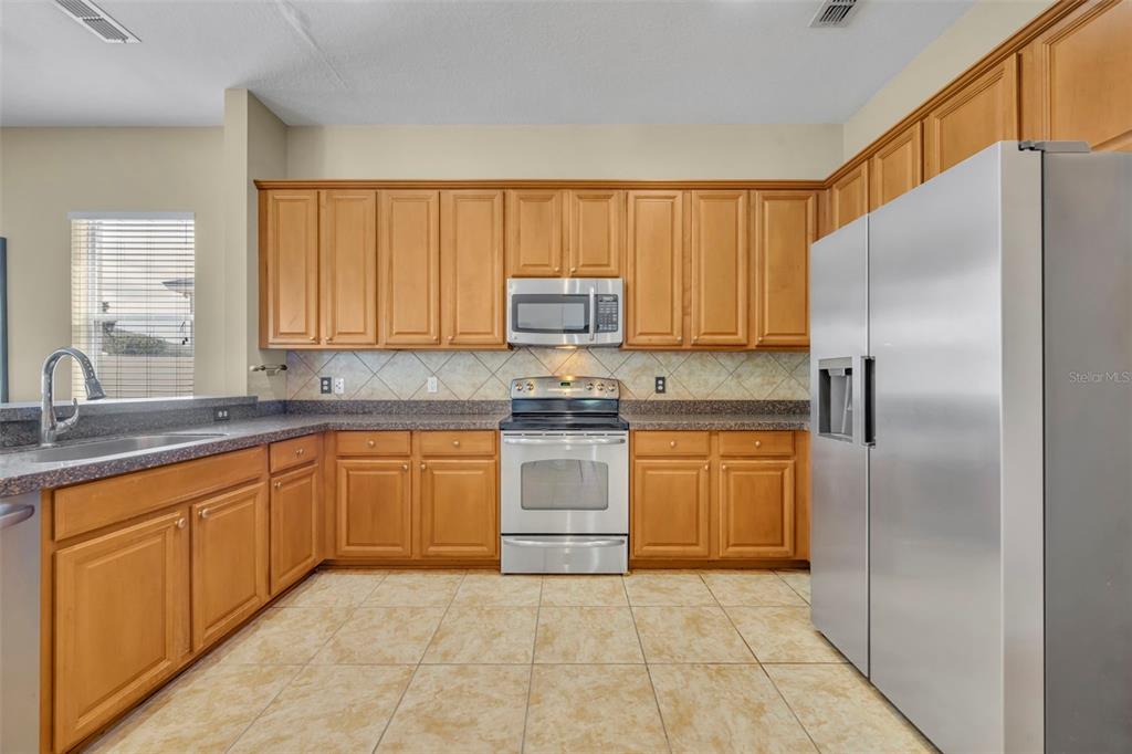 A kitchen features wood cabinets, stainless steel appliances, dark countertops, and light-colored tile flooring — 5459 RISHLEY RUN WAY, MOUNT DORA, FL
