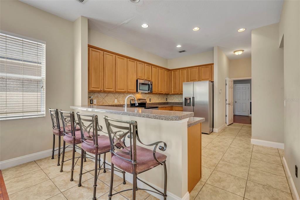 A kitchen with light wood cabinets, granite countertops, a breakfast bar, and tile flooring — 5459 RISHLEY RUN WAY, MOUNT DORA, FL