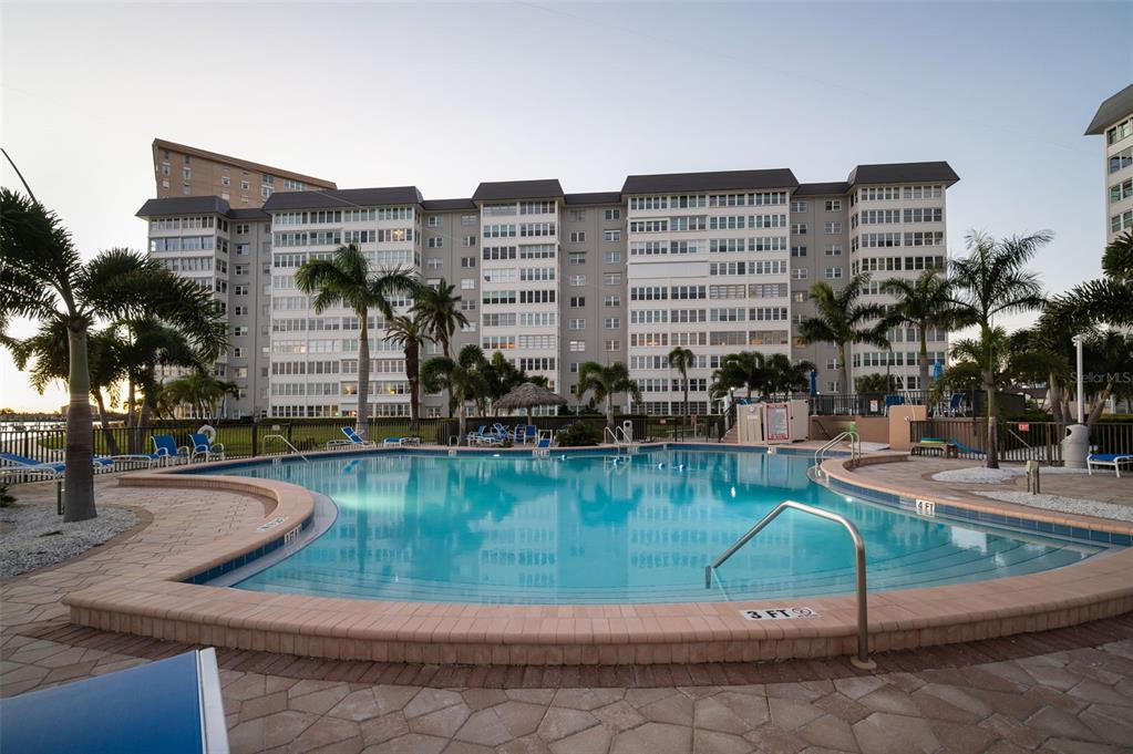 A swimming pool with a brick deck sits in front of a large apartment building — 5130 BRITTANY DRIVE S UNIT 202, ST PETERSBURG, FL