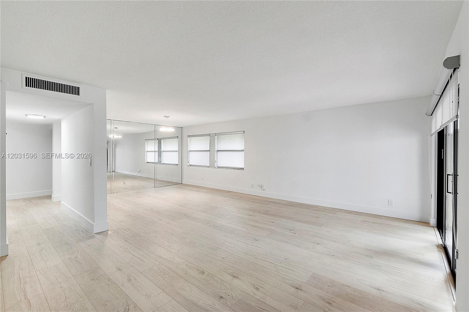 An empty, white-walled living room features light wood-look flooring and a large mirrored wall — 398 Fern Dr # 6, Weston FL 33326, WESTON, FL