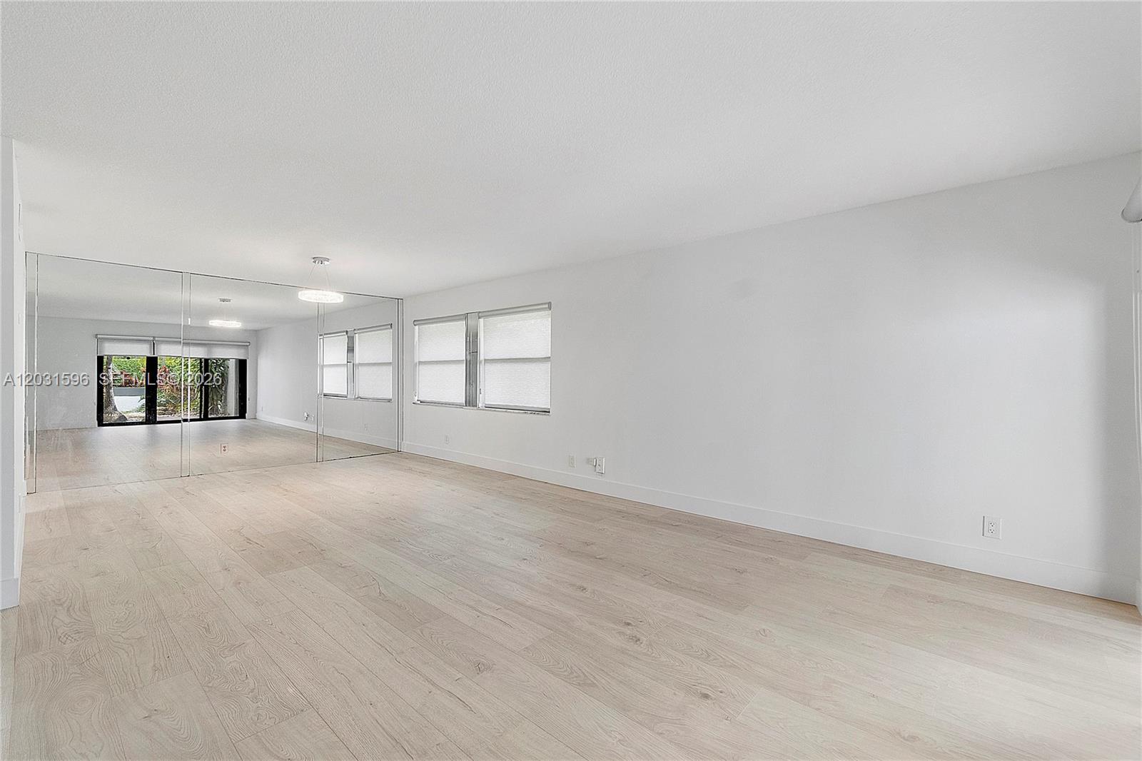 A bright, empty room features light wood flooring, white walls, and a large mirrored wall — 398 Fern Dr # 6, Weston FL 33326, WESTON, FL