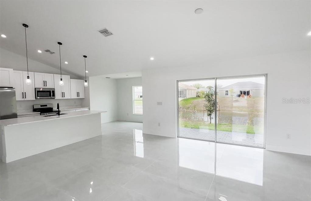A modern kitchen and living area with white cabinets, tile floors, and sliding glass doors — 2906 NW 22ND AVENUE, CAPE CORAL, FL
