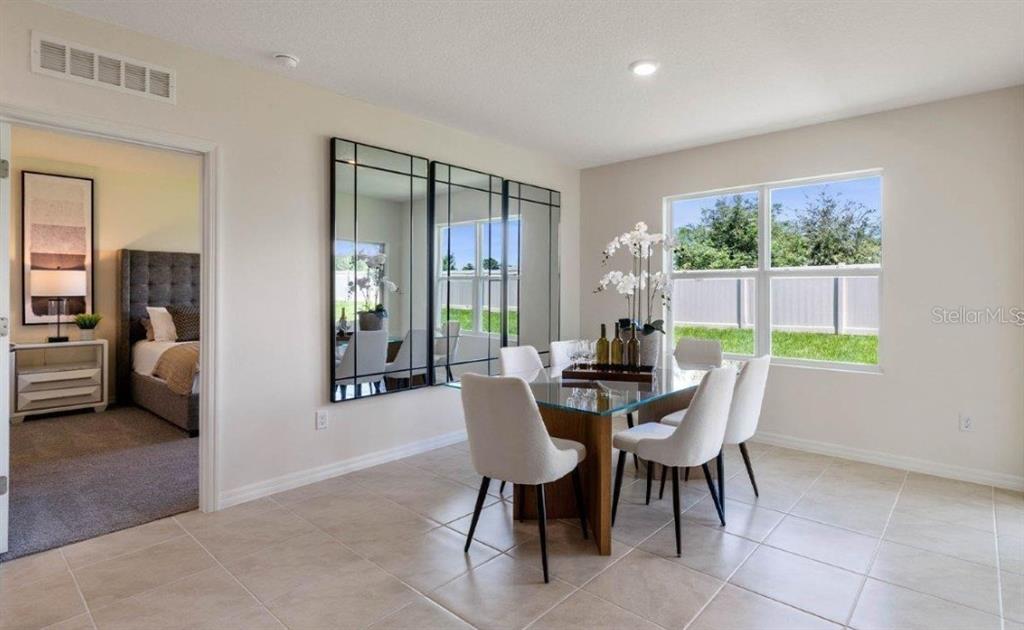 A dining room features a glass-top table, white chairs, large wall mirrors, and tile flooring — 1827 SILVERBELL LOOP, HAINES CITY, FL