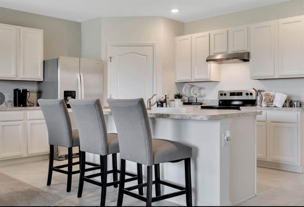 A kitchen features white cabinets, a granite-topped island, and three gray bar stools — 1827 SILVERBELL LOOP, HAINES CITY, FL