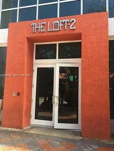 The exterior entrance of a building features orange stucco walls and double glass doors — 133 NE 2nd Ave # 1103, Miami FL 33132, MIAMI, FL