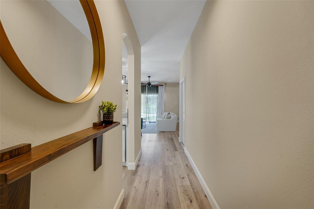 A hallway with wood-look flooring leads to a living area with a white sofa — 1111 LONG OAK WAY, SANFORD, FL