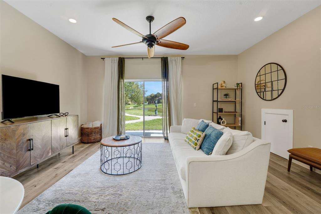 A living room features a white sofa, wood-toned media console, ceiling fan, and sliding glass doors — 1111 LONG OAK WAY, SANFORD, FL