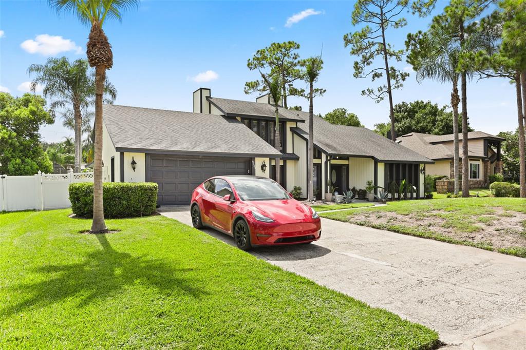 A red Tesla is parked in the driveway of a two-story house with light siding — 9524 BAY VISTA ESTATES BOULEVARD, ORLANDO, FL