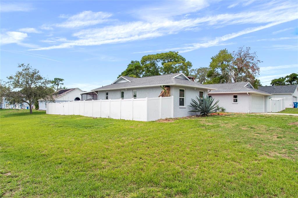 A light-colored house with a white vinyl fence and a detached garage on a lawn — 2327 EVA AVENUE, SPRING HILL, FL