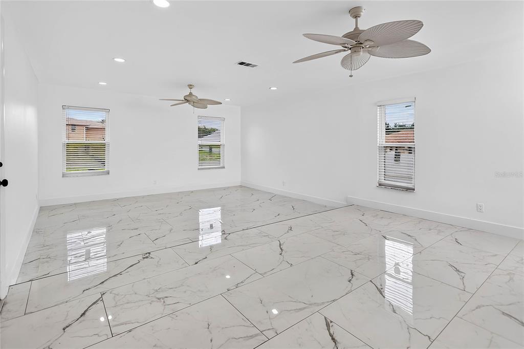 A bright, empty room features white walls, recessed lighting, two ceiling fans, and marble-look tile — 2327 EVA AVENUE, SPRING HILL, FL