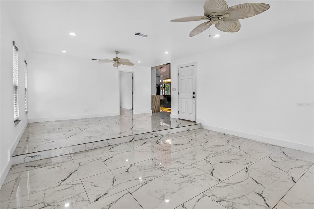 A living room with white walls, a sunken floor, and white marble-look tile flooring — 2327 EVA AVENUE, SPRING HILL, FL