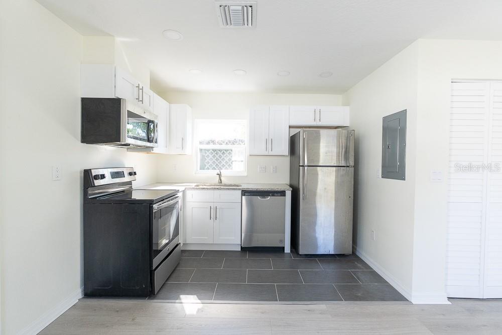 A kitchen features white cabinets, stainless steel appliances, a black stove, and gray tile flooring — 3520 1/2 8TH AVENUE N, ST PETERSBURG, FL
