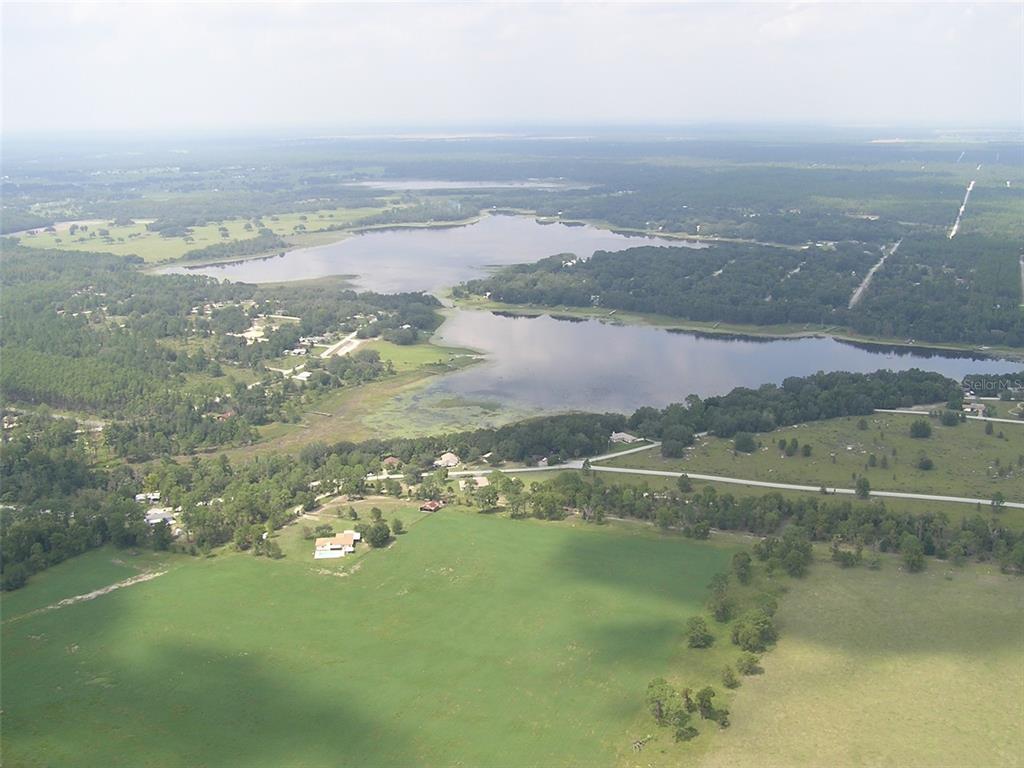 An aerial view shows a large lake surrounded by rural landscape, trees, and scattered houses — Lot 22 SW RAINBOW LAKES BOULEVARD, DUNNELLON, FL