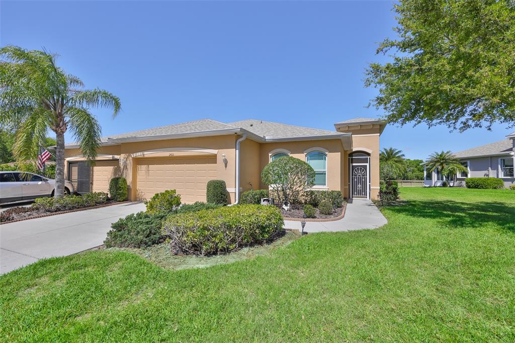 A single-story tan house with a two-car garage, arched windows, and a landscaped front yard — 2423 RICHMOND GREENS COURT, SUN CITY CENTER, FL
