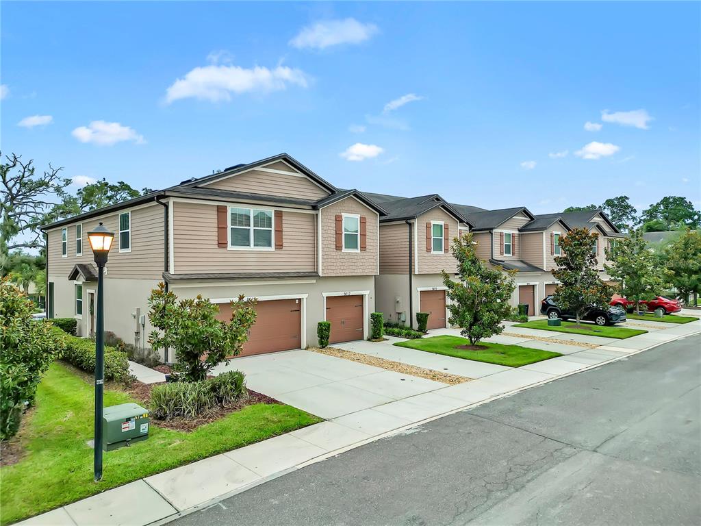 A row of two-story townhomes with tan siding, brown garage doors, and small front lawns — 5019 BLUE LATAN LANE, TAMPA, FL