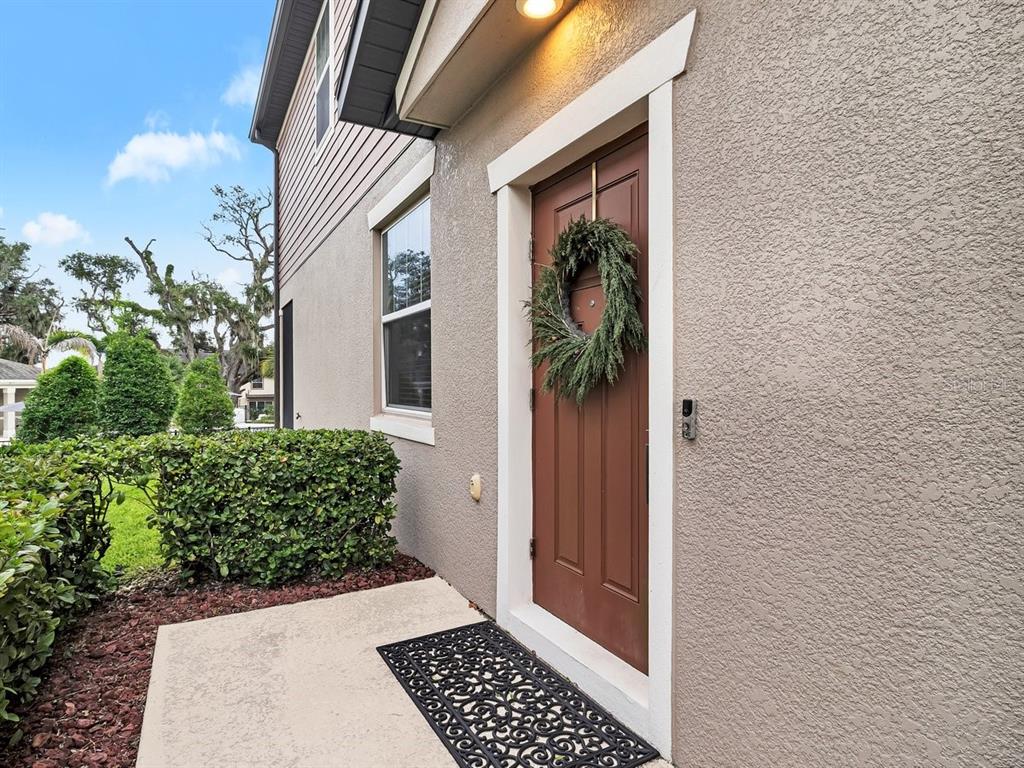 A brown front door with a wreath is set into a beige stucco exterior wall — 5019 BLUE LATAN LANE, TAMPA, FL