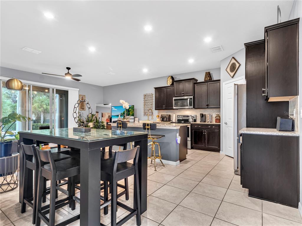 A kitchen with dark cabinets, a granite-topped island, and a dining table on tile flooring — 5019 BLUE LATAN LANE, TAMPA, FL