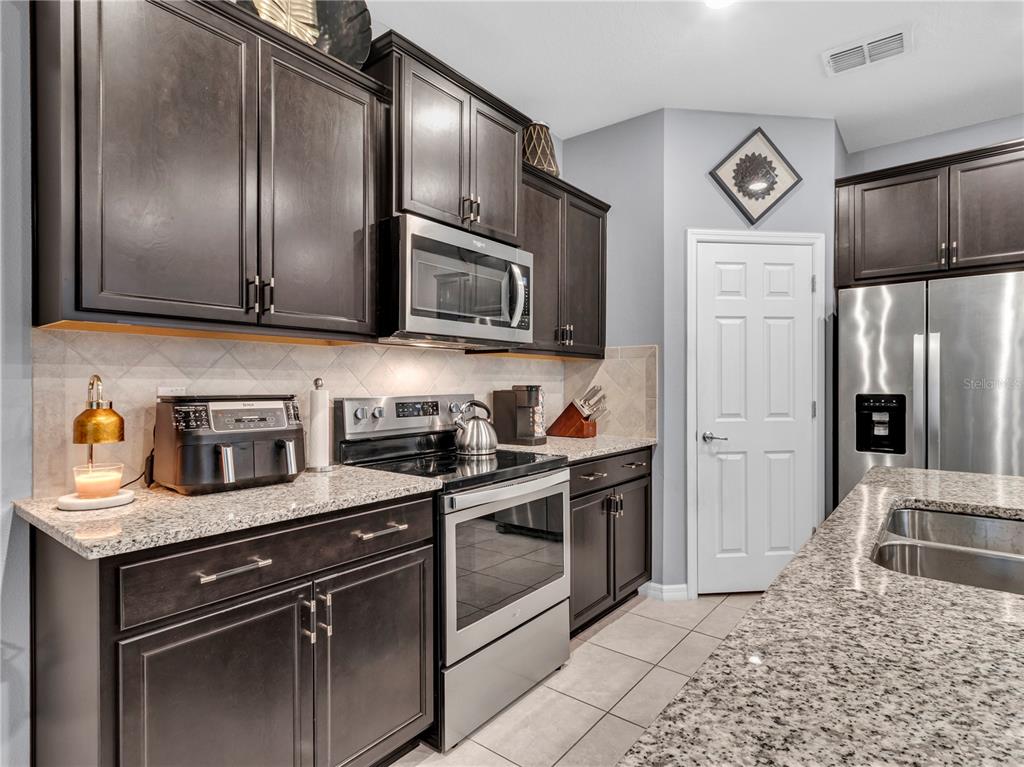 A kitchen features dark wood cabinets, granite countertops, stainless steel appliances, and tile flooring — 5019 BLUE LATAN LANE, TAMPA, FL
