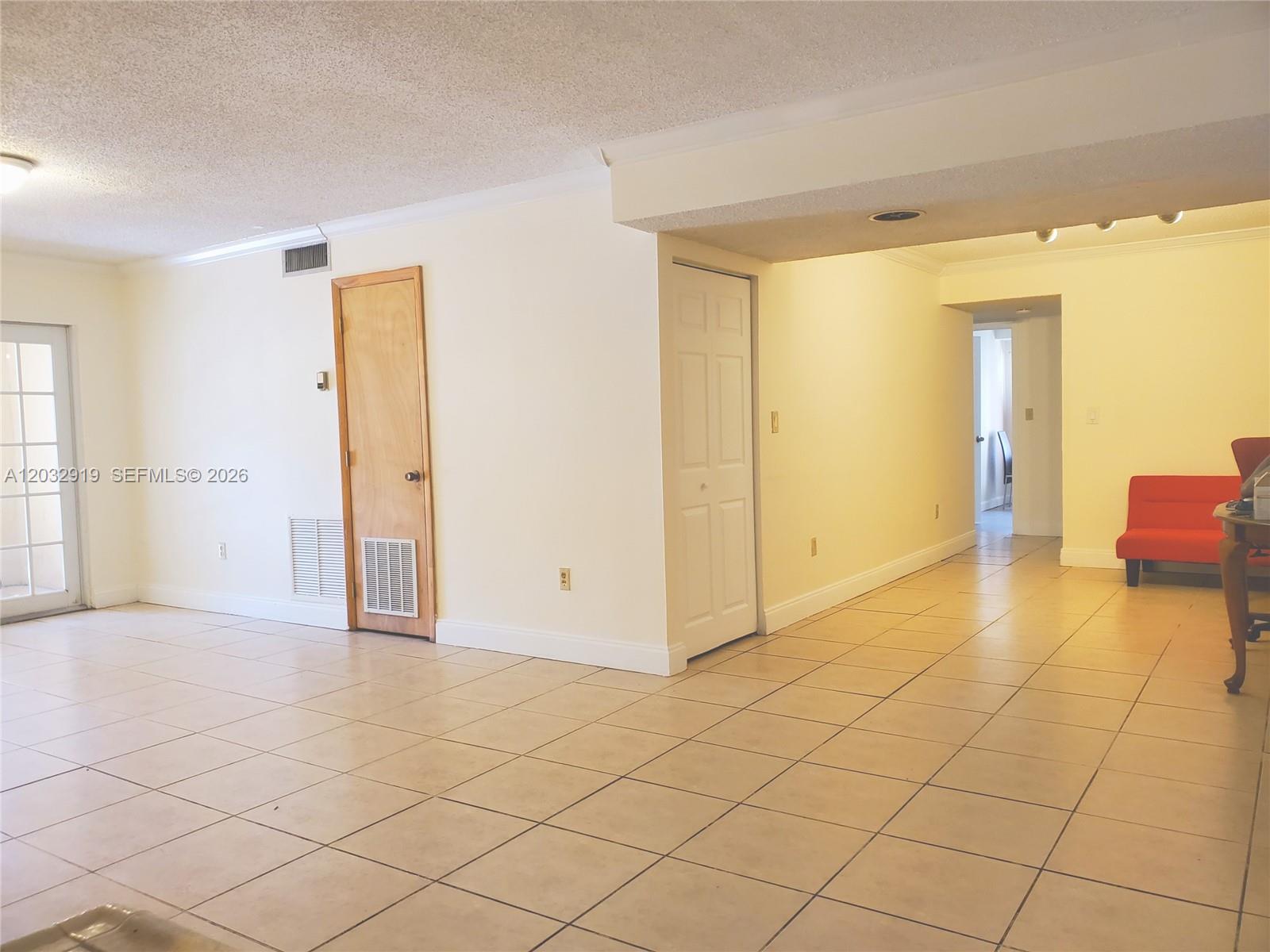 A tiled living area features a wooden door, a white closet, and a red chair — 250 NW 107th Ave # 106, Miami FL 33172, MIAMI, FL