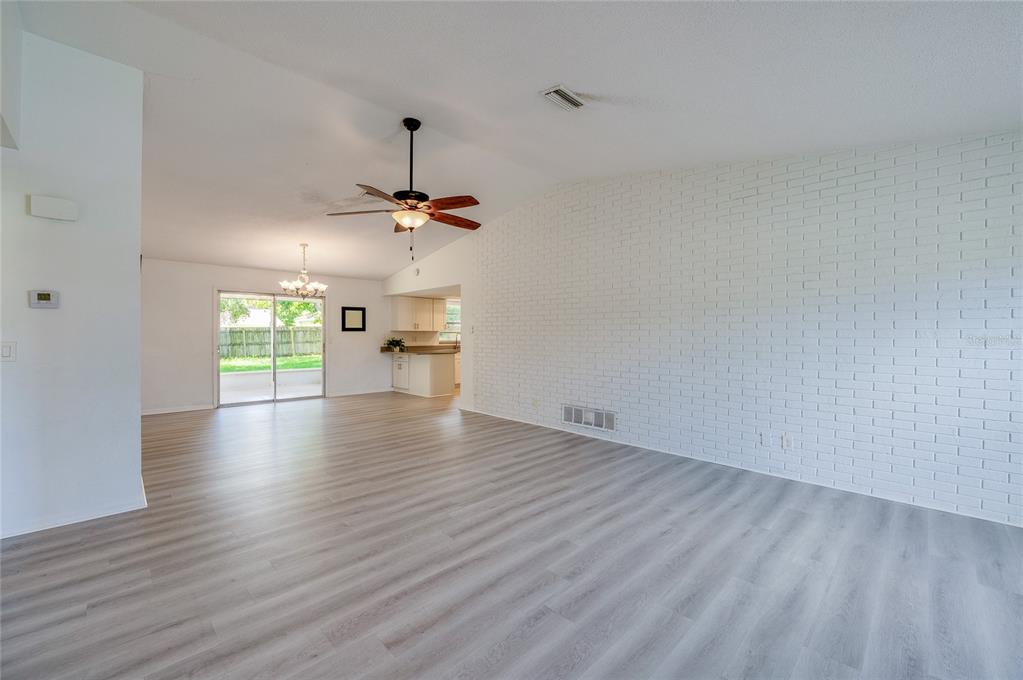 A spacious living room features light wood-look flooring and a large white brick accent wall — 156 SPRINGWOOD DRIVE, DAYTONA BEACH, FL