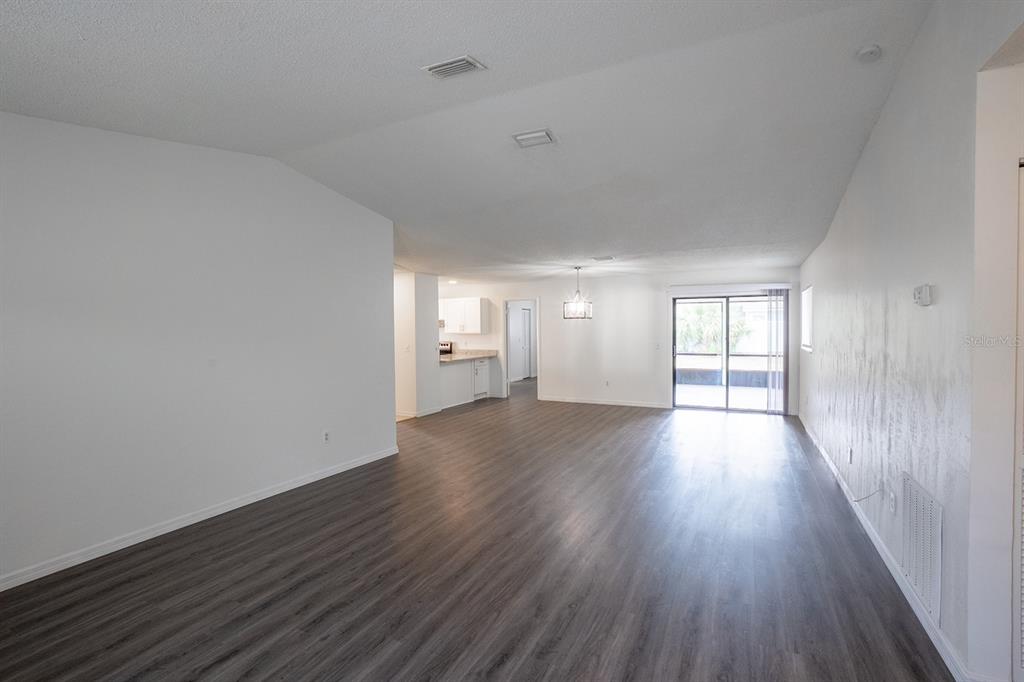 An open-concept living and dining area features wood-look flooring, white walls, and sliding glass doors — 13 WHITTINGTON DRIVE, PALM COAST, FL