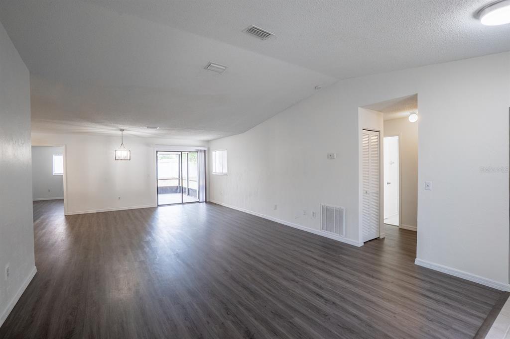 An open-concept living area features vaulted ceilings, gray wood-look flooring, and a sliding glass door — 13 WHITTINGTON DRIVE, PALM COAST, FL