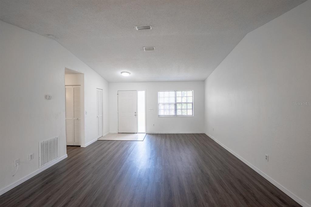 An empty living room features white walls, dark wood-look flooring, and a front entry door — 13 WHITTINGTON DRIVE, PALM COAST, FL