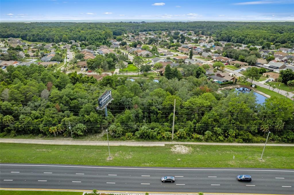 An aerial view shows a highway in the foreground bordering a wooded area and residential neighborhood — 00 US HWY 19, HUDSON, FL