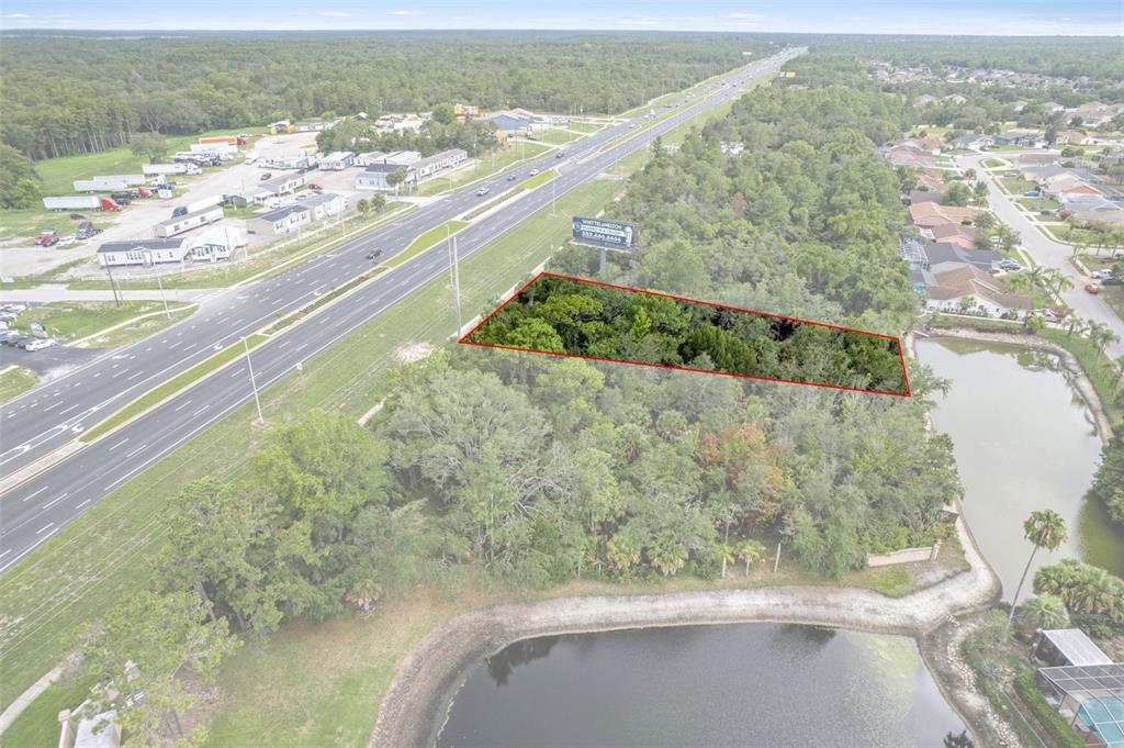 An aerial view shows a wooded lot outlined in red next to a highway and pond — 00 US HWY 19, HUDSON, FL