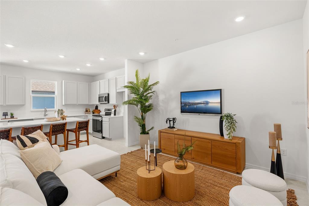 A bright open-concept living room features a white sectional sofa, wooden coffee tables, and kitchen — 731 BLISSFUL GARDENS WAY, APOPKA, FL
