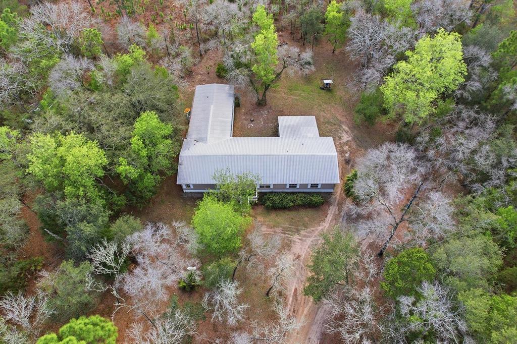 An aerial view shows an L-shaped house with a metal roof surrounded by wooded land — 4950 W MOCKINGBIRD STREET, HOMOSASSA, FL