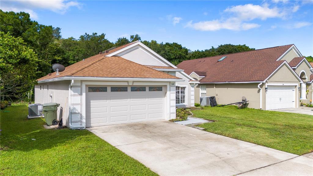 A single-story house with a brown shingled roof, beige stucco walls, and a two-car garage — 2016 LOCUST BERRY DRIVE, KISSIMMEE, FL