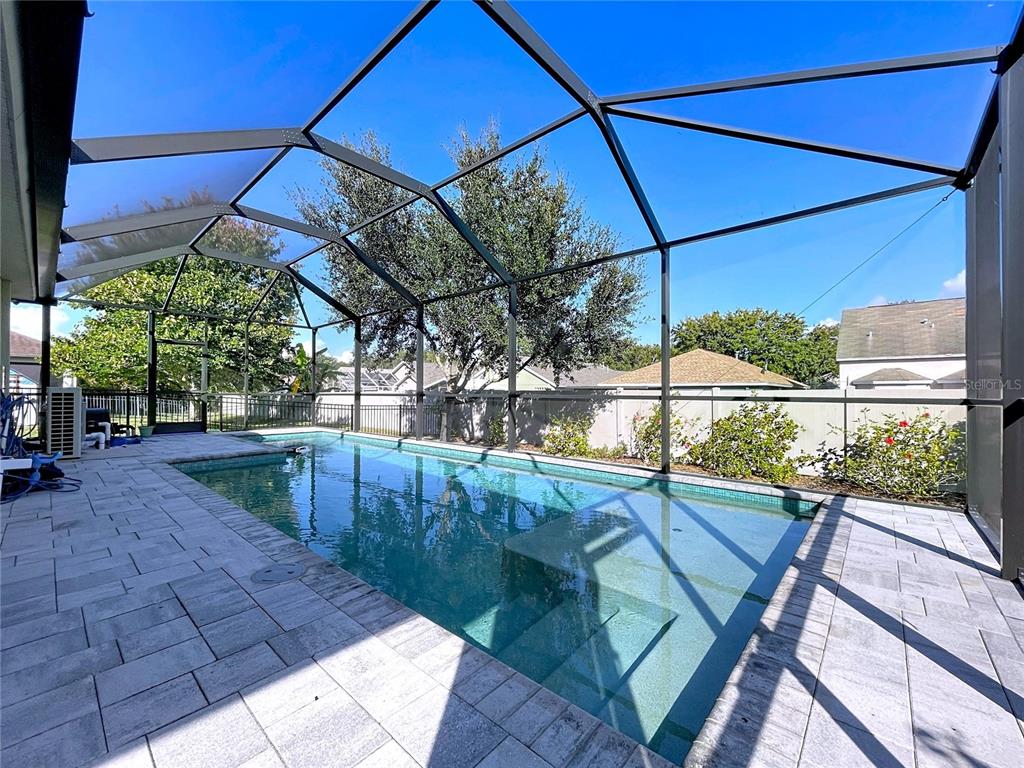 A rectangular swimming pool is enclosed by a screened lanai with light-colored stone pavers — 6507 NESTALL COURT, APOLLO BEACH, FL