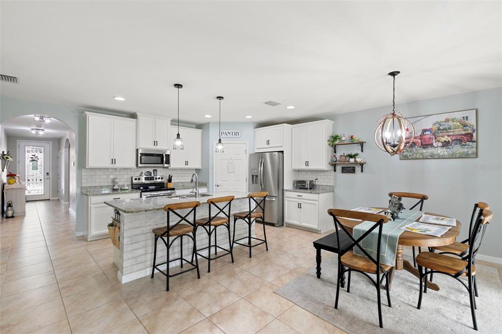 A kitchen features white cabinets, a granite-topped island with bar stools, and an adjacent dining area — 3215 BIRCHIN LANE, FORT MYERS, FL