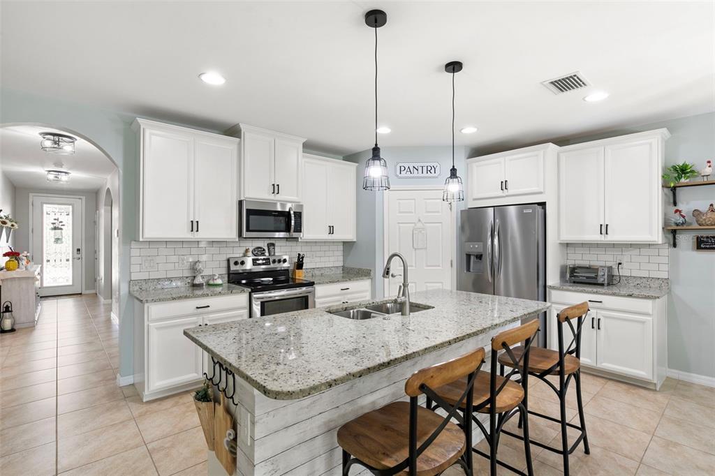 A kitchen features white cabinets, granite countertops, a central island with bar stools, and tile flooring — 3215 BIRCHIN LANE, FORT MYERS, FL