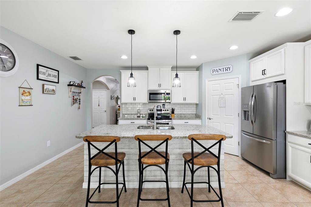 A kitchen features white cabinets, a granite-topped island with three stools, and stainless steel appliances — 3215 BIRCHIN LANE, FORT MYERS, FL