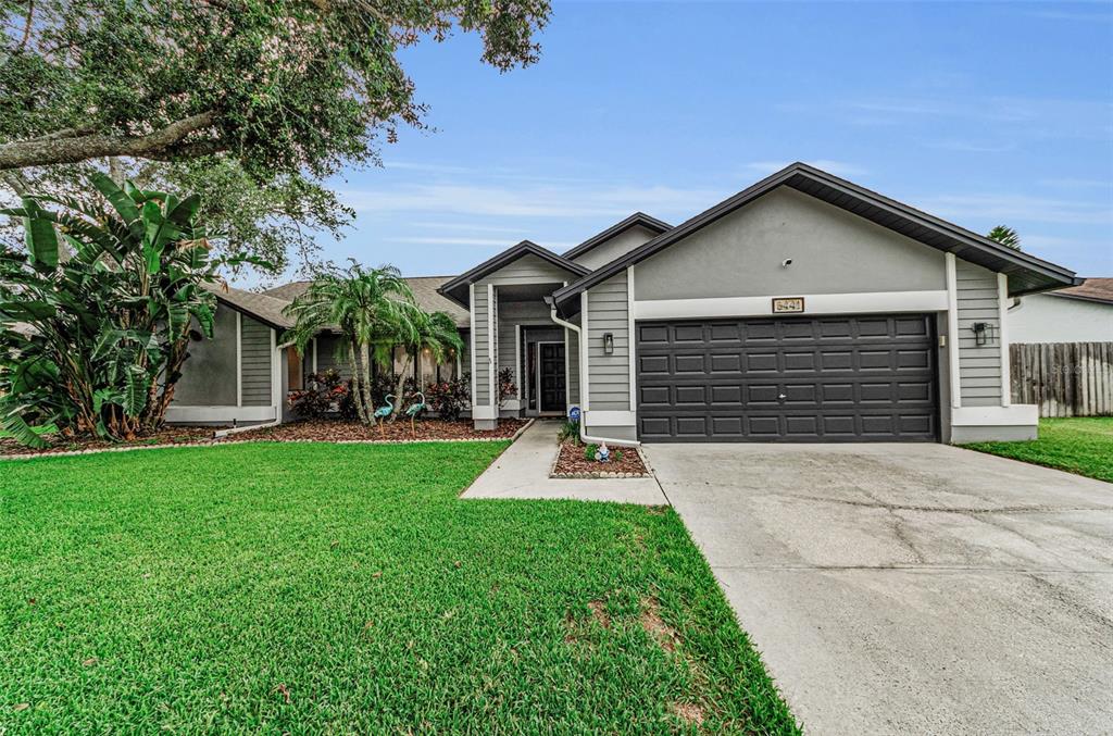 A single-story house with gray siding, a dark garage door, and a green lawn — 5441 WORTHINGTON LOOP, PALM HARBOR, FL