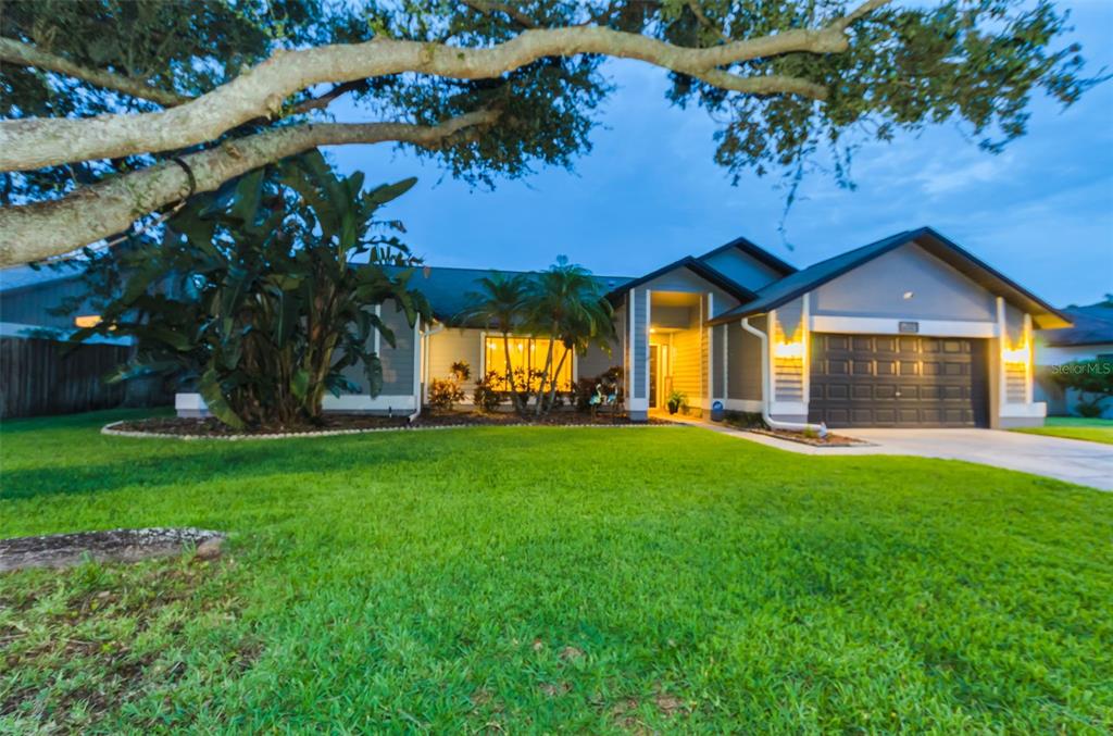 A single-story house with a two-car garage, a large tree, and landscaping at dusk — 5441 WORTHINGTON LOOP, PALM HARBOR, FL