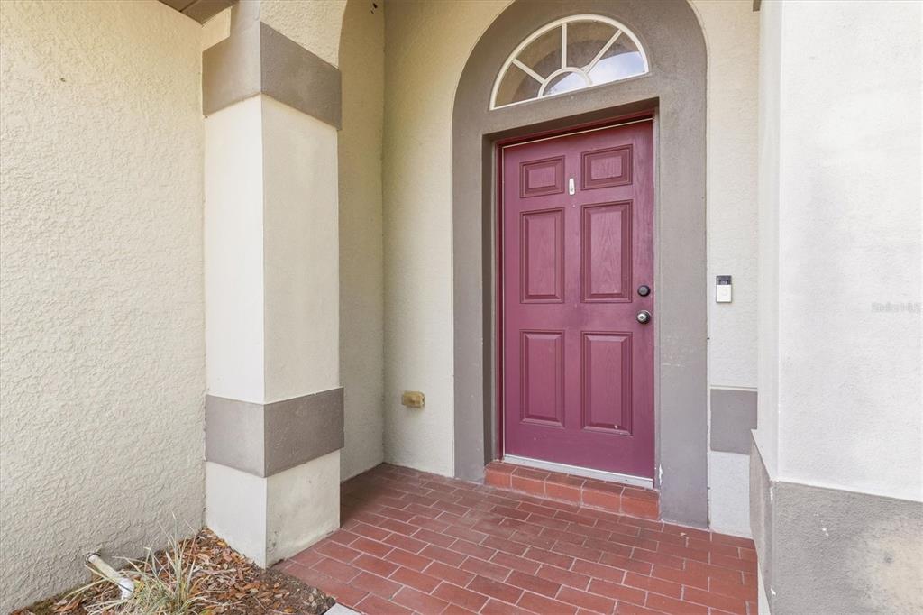A red front door with a transom window sits within a covered brick entryway — 3036 GIANNA WAY, LAND O LAKES, FL