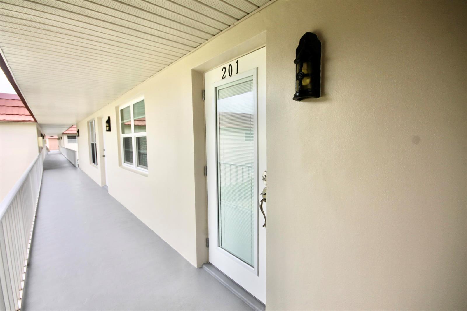 An exterior walkway leads to a white door labeled 201 with a wall-mounted light fixture — 26 Pine Arbor Lane # 201, Vero Beach FL 32962, VERO BEACH, FL