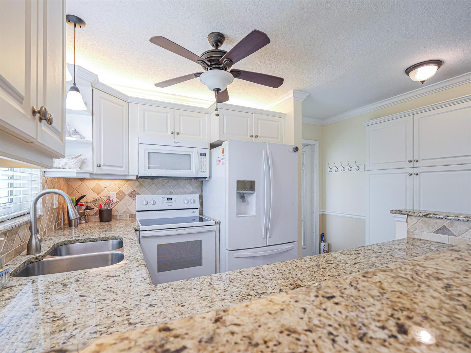 A kitchen features white cabinets, granite countertops, stainless steel appliances, and a ceiling fan — 26 Pine Arbor Lane # 201, Vero Beach FL 32962, VERO BEACH, FL