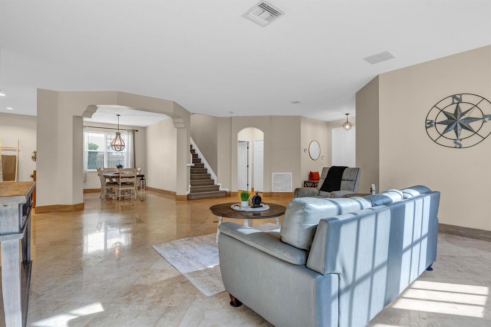 A living room with tile floors, a grey sofa, and a staircase in the background — 2792 Shaughnessy Drive, Wellington FL 33414, WELLINGTON, FL